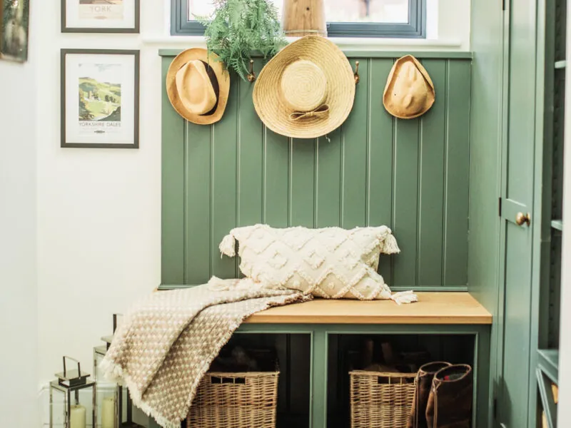 Boot room in green with hats hanging above a bench